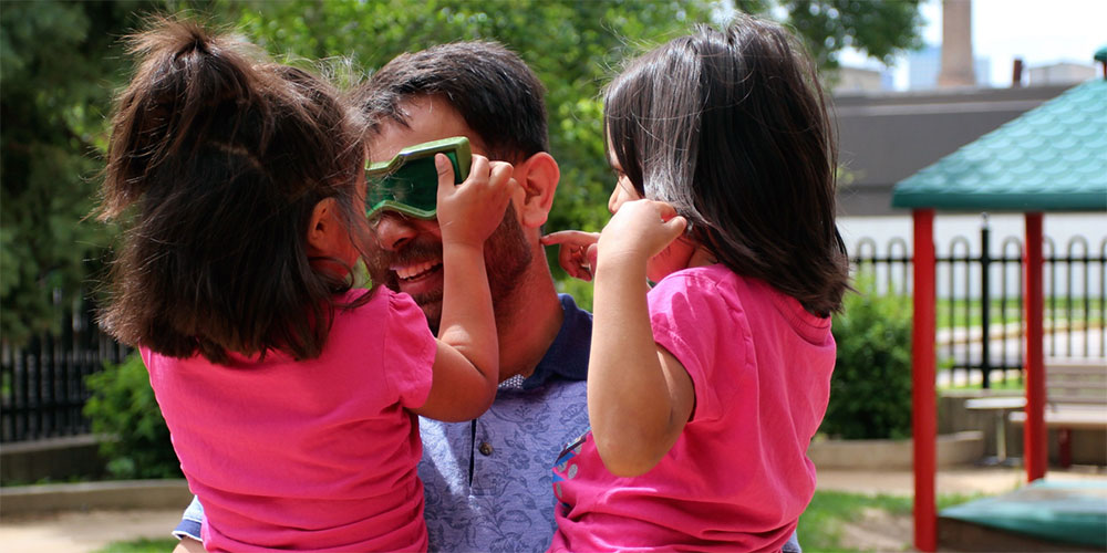 Man with green glasses holding two young girls.